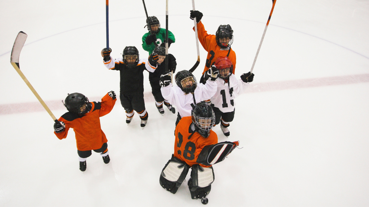Young hockey players lifting their sticks in the sky in enjoyment.